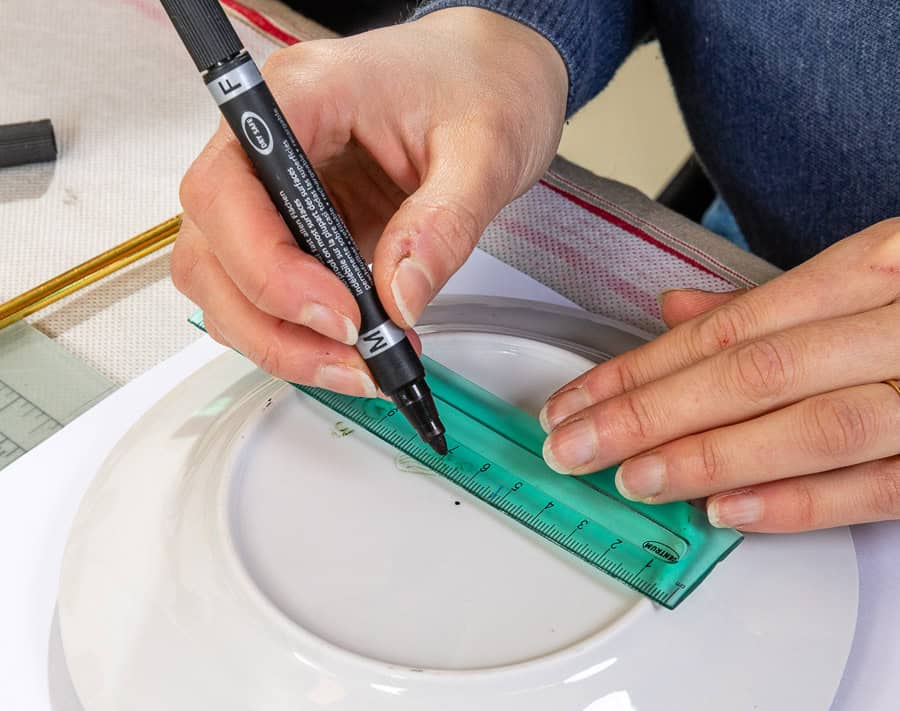 Käsitsi joonistab joonlaua abil disaini kandikule.